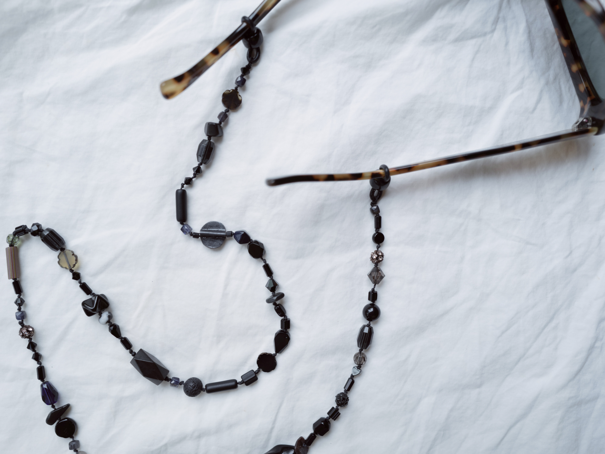 Black glasses chain with tortoise shell sunglasses on white linen